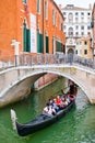 Gondola carrying tourists under a bridge on a narrow canal in Venice