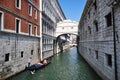 A gondola with tourists floats along the narrow canal of Venice. View of the walls of the houses and the bridge between the houses