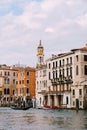 A gondola with tourists is sailing along the Grand Canal amid the facades of Venetian houses standing on the water in Royalty Free Stock Photo