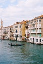 A gondola with tourists is sailing along the Grand Canal amid the facades of Venetian houses standing on the water in Royalty Free Stock Photo