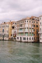 A gondola with tourists is sailing along the Grand Canal amid the facades of Venetian houses standing on the water in Royalty Free Stock Photo