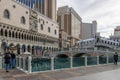 Gondolas docked along the blue waters and people walking along the sidewalk surrounded by hotels at The Venetian Hotel and resort