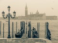 Gondolas moored by Saint Mark square and lamppost with San Giorgio di Maggiore church in the background at foggy day, vintage