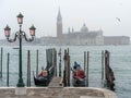 Gondolas moored by Saint Mark square and lamppost with San Giorgio di Maggiore church in the background at foggy day. Venice,