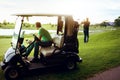 Gone golfing. a man watching his friend play golf while sitting in a golf cart.