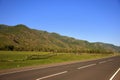 A good asphalt road running at the foot of a green hill along a fertile valley. Landscape