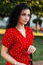 Good beautiful Italian girl with a curly hairstyle in a fashionable retro red dress is walking in the city