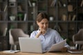 Satisfied millennial female reading paper documents before computer screen