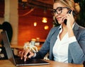 woman in glasses talking on mobile phone and using laptop with smile while sitting at her working place. Royalty Free Stock Photo