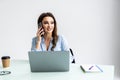 Good business talk. Cheerful young woman in glasses talking on mobile phone and using laptop with smile while sitting at her Royalty Free Stock Photo