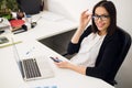 Good business talk. Cheerful young beautiful woman in glasses talking on mobile phone and using laptop with smile while Royalty Free Stock Photo