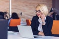 Good business talk. Cheerful young beautiful woman in glasses talking on mobile phone and using laptop Royalty Free Stock Photo