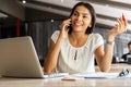 Good business talk. Cheerful young beautiful woman talking on mobile phone and using laptop with smile while sitting at