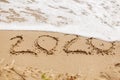 Good bye 2020 ! Wave with foam covering 2020 sign on sandy beach, leaving awful year 2020 Royalty Free Stock Photo