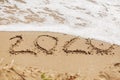 Good bye 2020 ! Wave with foam covering 2020 sign on sandy beach, leaving awful year 2020 Royalty Free Stock Photo