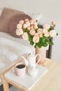 Good cozy morning. Bouquet of rose flowers in vase on table. Hotel room with bed. Check in hotel. Rest and relaxation. Coffee in