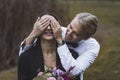 Good-humored young attractive Scandinavian groom in elegant white shirt covering the eyes of his newlywed Turkish wife