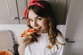 Good-humoured girl eating pizza in kitchen. Close-up shot of positive woman enjoying her dinner. Royalty Free Stock Photo