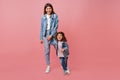 Good-humoured mom and daughter in denim jackets having fun together. Young mother and child holding hands on pink Royalty Free Stock Photo