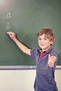 Good job. a little boy showing thumbs up while writing on the blackboard during a lesson. Royalty Free Stock Photo