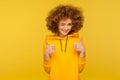 Good job! Portrait of optimistic curly-haired young woman in urban style hoodie winking and showing thumbs up