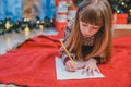 Little girl, sure that she behaved good the whole year, is writing a letter to Santa to get the present.