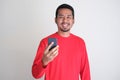 Good looking adult Asian man wearing plain red clothes smiling confident while holding a handphone Royalty Free Stock Photo