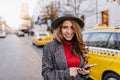 Good-looking businesslady in gray hat gently smiling, walking down the road. Stunning dark-haired female model in coat