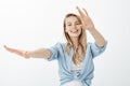 Good-looking carefree fair-haired woman in stylish clothes, dancing and pulling hands towards camera while smiling