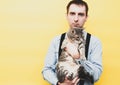 Man in blue shirt and black suspender holding cute tabby grey cat and looking at camera