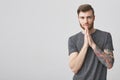 Good-looking european manly guy with ginger beard, dark hair and tattoo on left arm holding palms together with