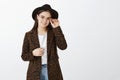 Good-looking fashionable european girl in glasses, hat and coat with leopard print, touching rim of eyewear and smiling
