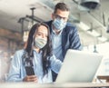 Good looking female and male coworkers look at the computer screen together, wearing face masks Royalty Free Stock Photo