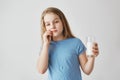 Good-looking funny blonde girl with blue eyes holding glass, stroking milk mustache with hand making sneaky face Royalty Free Stock Photo