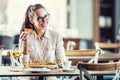 Good-looking girl in glasses sits in a restaurant holding a slice of pizza in her hand, having a glass of wine, smiling Royalty Free Stock Photo