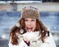 Good looking Girl in Winter Clothing blows white Snow and smiles in front of a wooden barn with lots of snow falling from the sky Royalty Free Stock Photo