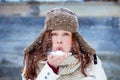 Good looking Girl in Winter Clothing blows white Snow and smiles in front of a wooden barn with lots of snow falling from the sky Royalty Free Stock Photo