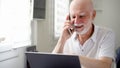 Senior man sitting at home with laptop and smartphone. Using cellphone discussing project on screen Royalty Free Stock Photo