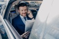 Good looking young executive manager in formal wear reads newspaper on backseat of car