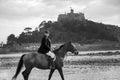 Good Looking Male Horse Rider riding horse on beach in traditional riding clothing with St Michael`s Mount in background Royalty Free Stock Photo