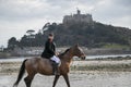 Good Looking Male Horse Rider riding horse on beach in traditional riding clothing with St Michael`s Mount in background Royalty Free Stock Photo