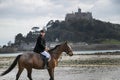 Good Looking Male Horse Rider riding horse on beach in traditional riding clothing with St Michael`s Mount in background Royalty Free Stock Photo