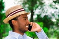 Good looking man wearing blue shirt and summer hat talking on mobile phone while enjoying beautiful day in park Royalty Free Stock Photo