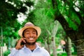 Good looking man wearing blue shirt and summer hat talking on mobile phone while enjoying beautiful day in park Royalty Free Stock Photo