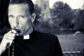 Good looking priest kisses his rosary with church, field and alpaca in background Royalty Free Stock Photo