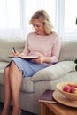 Good-looking ripened female writing letter while sitting on sofa Royalty Free Stock Photo