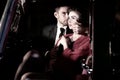 Good looking couple, handsome man in suit, beatiful woman in red dress, embrace passionately in vintage car Royalty Free Stock Photo