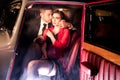 Good looking couple, handsome man in suit, beatiful woman in red dress, embrace passionately in vintage car Royalty Free Stock Photo