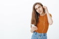 Good-looking stylish female blogger in trendy outfit, taking off earphone while tilting head and listening music Royalty Free Stock Photo