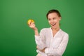 A good-looking woman of forty in a white shirt on a green background smiles and holds a fresh apple in her hands. Healthy eating, Royalty Free Stock Photo